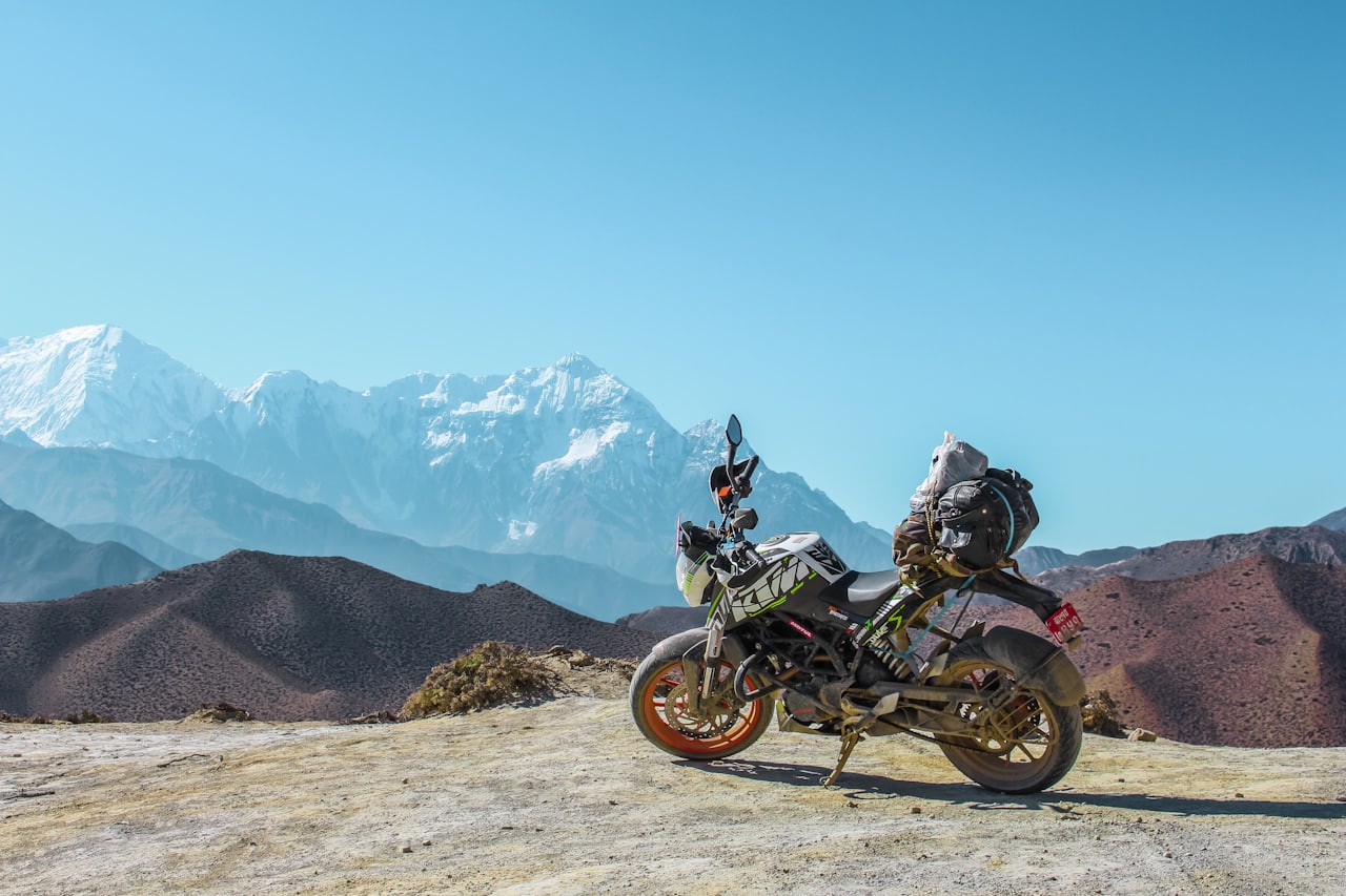 A dust-covered adventure motorcycle parked on a remote red dirt outback road under a shimmering heat haze