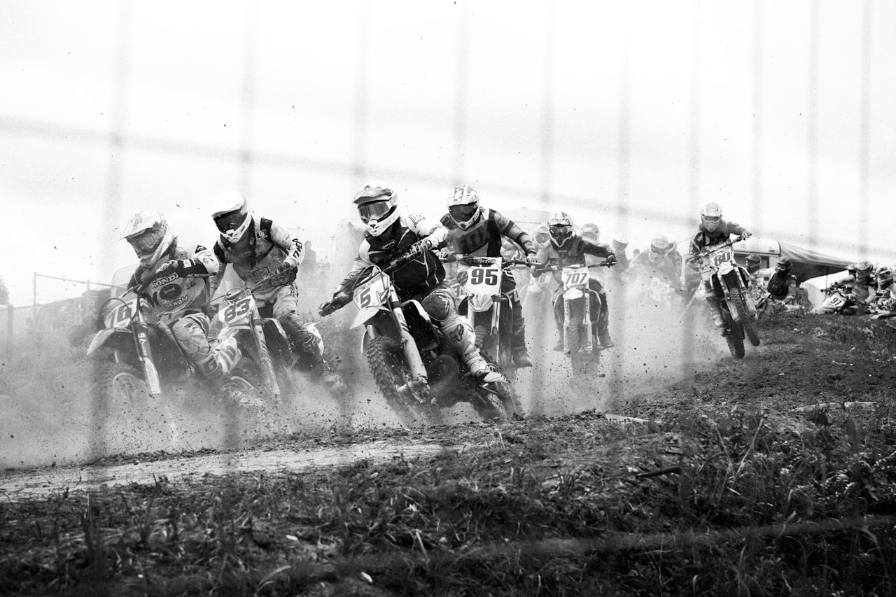 A motorcycle's rear tyre cutting through standing water on wet asphalt at dusk, spray kicking up behind the wheel
